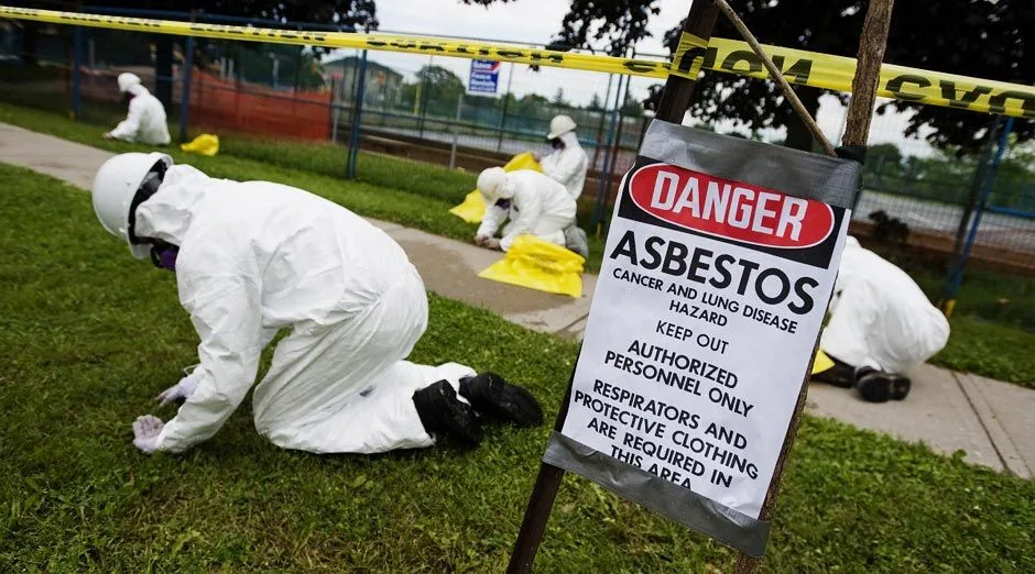 Asbestos clean-up crew in white protective suits behind a DANGER asbestos warning sign
