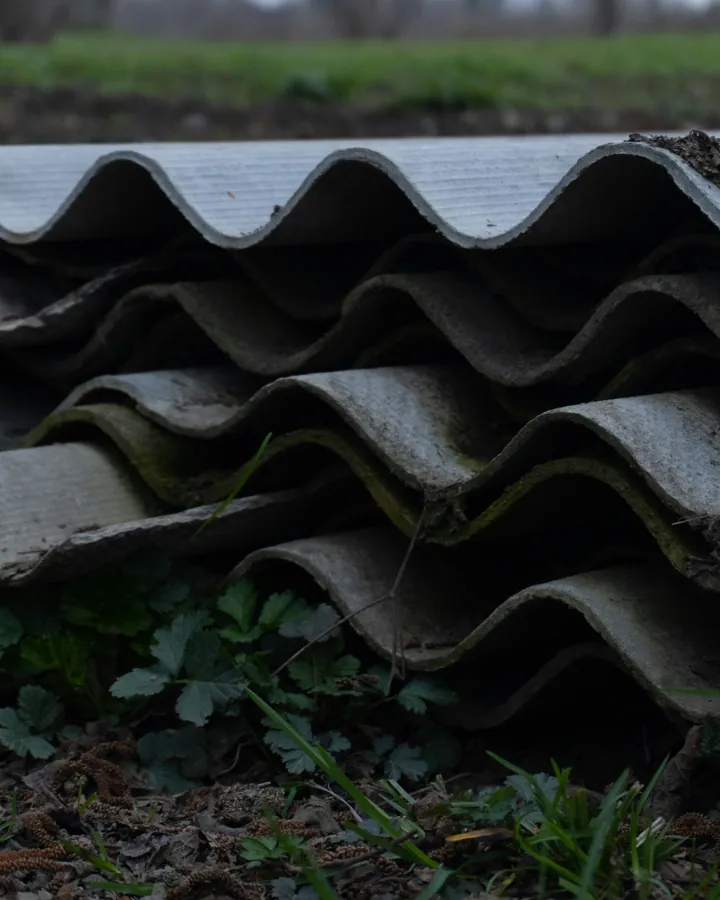 Stack of weathered corrugated cement roof sheets lying on the ground